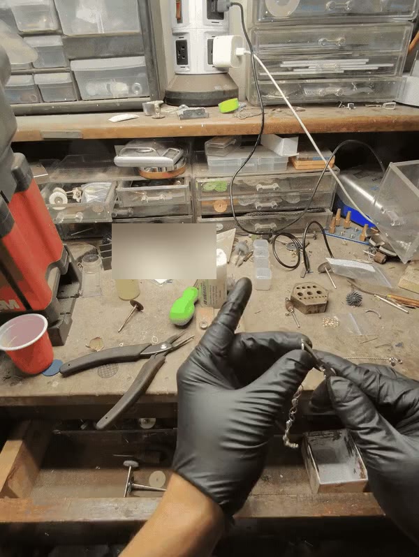 First-person view of a goldsmith assembling a chain at the bench.